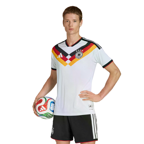 A person in a German national team soccer uniform poses with a soccer ball against a black background.