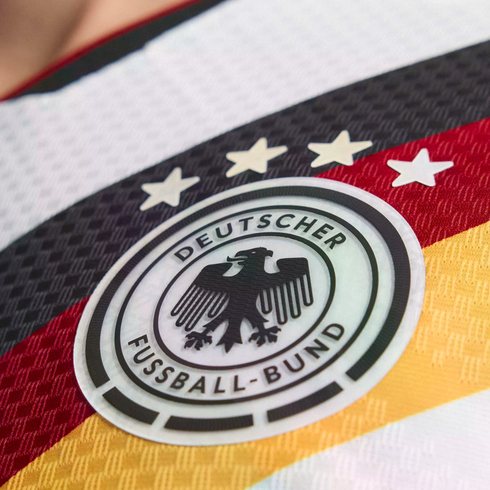 Close-up of the Germany national football team crest on a jersey. The circular logo features an eagle and four stars above black, red, and gold stripes.