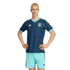 A man models a navy blue and teal German national team soccer kit, standing with hands on his hips against a solid black background.