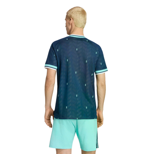 Rear view of a person with blonde hair in a patterned navy blue jersey and mint green athletic shorts, standing against a black background.
