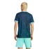 Rear view of a person with blonde hair in a patterned navy blue jersey and mint green athletic shorts, standing against a black background.