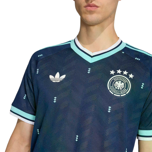 Man wearing a navy blue German soccer jersey with an Adidas trefoil logo, national team crest, and teal trim on the collar and sleeves.