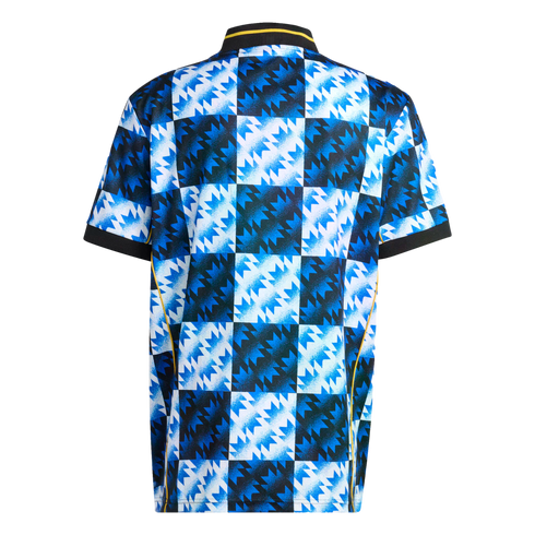 Back view of a jersey with a blue, white, and black checkerboard pattern and jagged geometric shapes. Features a black ribbed collar and cuffs with yellow trim.