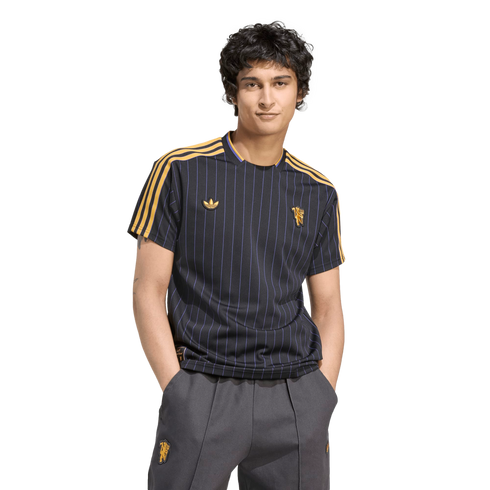 A man models a navy pinstriped Manchester United jersey and grey trousers against a black background.