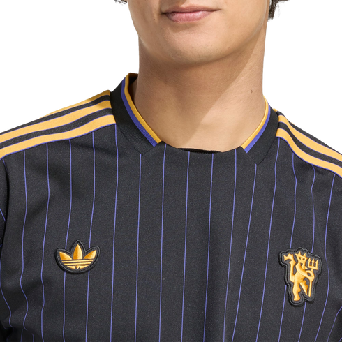 Close-up of a black jersey with purple pinstripes, gold shoulder stripes, an Adidas trefoil logo, and a Manchester United crest.