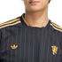 Close-up of a black jersey with purple pinstripes, gold shoulder stripes, an Adidas trefoil logo, and a Manchester United crest.