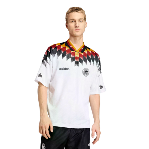 A man models a white Adidas Germany football jersey featuring a black, red, and yellow diamond pattern across the shoulders and neck.