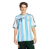 A young man with curly brown hair wearing a blue and white striped Argentina football jersey and black shorts against a black background.