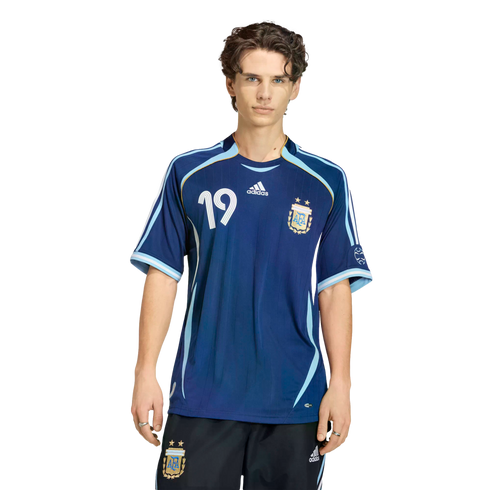 Young man posing in a dark blue Argentina soccer jersey with number 19 and matching shorts against a solid black background.