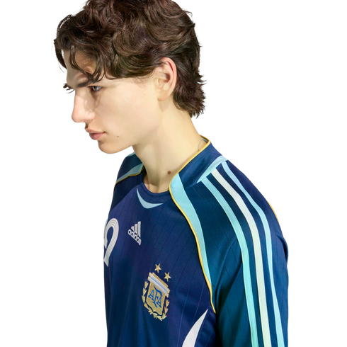 Profile of a young man with wavy brown hair wearing a navy blue Argentina national team soccer jersey against a solid black background.