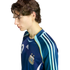 Profile of a young man with wavy brown hair wearing a navy blue Argentina national team soccer jersey against a solid black background.