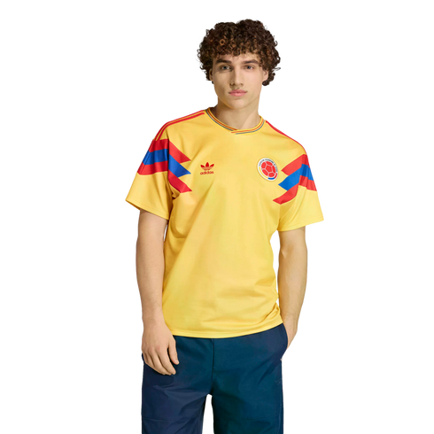 A man modeling a yellow Colombia national football team jersey with red and blue accents on the sleeves, standing against a black background.