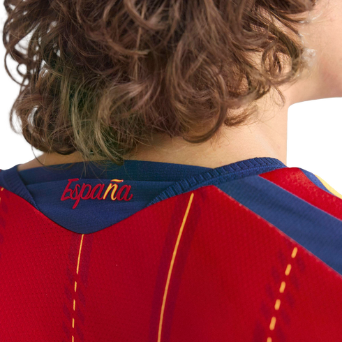 Close-up of the back of a person with curly hair wearing a red Spanish football jersey with "España" scripted on the blue neckline.