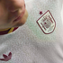 Close-up of a white Spain national team soccer jersey with a subtle ornate pattern, featuring a maroon RFEF crest and star, and an Adidas trefoil logo.