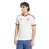 A man modeling a white Spain national football team jersey with red and yellow trim, paired with blue jeans, against a solid black background.