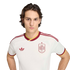 Young man with wavy brown hair in a white Spain national football team jersey with burgundy and yellow trim, against a black background.