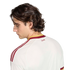 Profile of a man with wavy hair looking down, wearing a white Spanish soccer jersey with red shoulder stripes and "España" text, set against a black background.