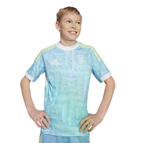 Smiling blonde boy in a light blue patterned Juventus soccer jersey with yellow shoulder stripes, posing with hands on hips against a white background.
