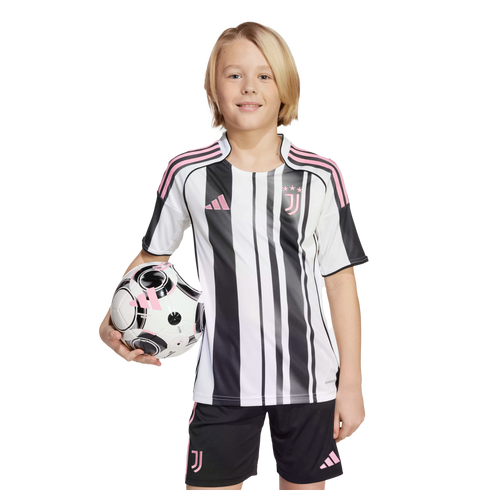 A smiling child with blonde hair wearing a black, white, and pink soccer uniform, holding a matching soccer ball under one arm against a white background.