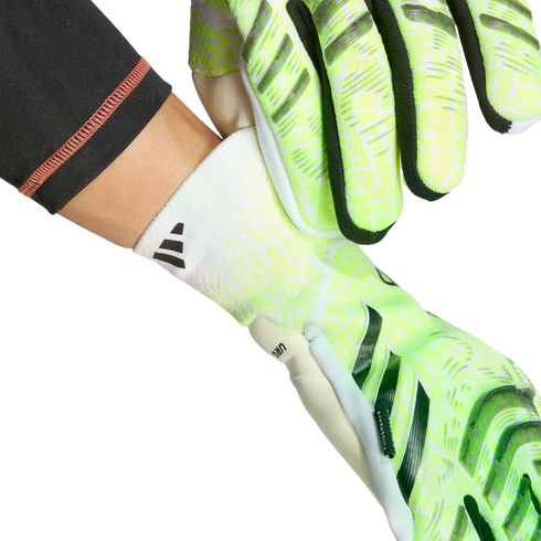 Hands putting on neon green and white Adidas goalkeeper gloves with white elasticated wrist cuffs.