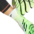 Hands putting on neon green and white Adidas goalkeeper gloves with white elasticated wrist cuffs.