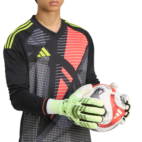 Goalkeeper in a black and red patterned Adidas jersey holds a soccer ball with lime green gloves against a black background.