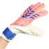 A pink and white Adidas Predator goalkeeper glove with blue accents, worn on a hand against a solid black background.