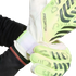 A person fastens the white velcro strap of a lime green and white Adidas Predator goalkeeper glove. The glove features dark grey textured patterns.