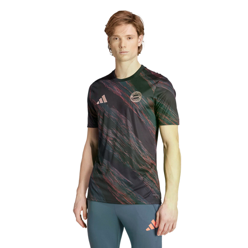A man models an Adidas FC Bayern Munich jersey with a dark pink and green brushstroke pattern and blue athletic leggings against a white background.