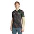 A man models an Adidas FC Bayern Munich jersey with a dark pink and green brushstroke pattern and blue athletic leggings against a white background.