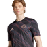 A man wearing a black FC Bayern Munich jersey with pink diagonal brushstroke patterns and the Adidas logo.