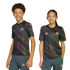A boy and a girl pose in matching black FC Bayern Munich soccer jerseys with a pink and green swirled pattern, standing against a white background.