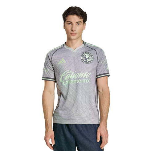 Man modeling a grey and mint green Club América soccer jersey with Adidas and Caliente.mx logos against a black background.