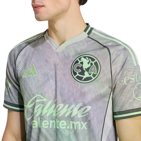 Close-up of a man wearing a grey and pale green Adidas Club América soccer jersey with the team crest and Caliente sponsor logo.