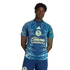 A Black man wearing a blue and yellow Club América soccer kit featuring intricate feather patterns and sponsor logos, posed against a plain black background.