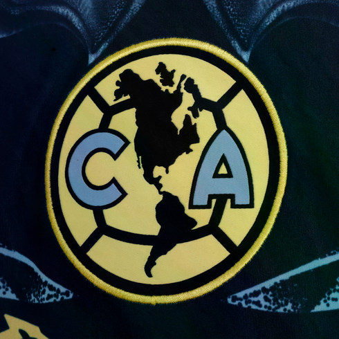 Club América logo: a yellow circle containing a black silhouette of the Americas, flanked by light blue letters "C" and "A" outlined in black.