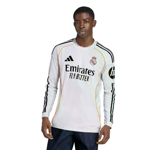 A young Black man models a white long-sleeved Real Madrid soccer jersey with black Adidas stripes and sponsor logos.