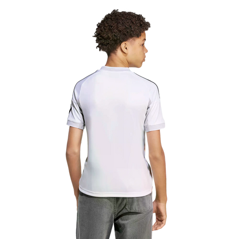 Back view of a youth with curly hair wearing a white athletic jersey with black shoulder stripes and grey jeans against a white background.