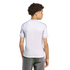 Back view of a youth with curly hair wearing a white athletic jersey with black shoulder stripes and grey jeans against a white background.