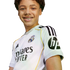 A smiling young boy with curly hair and braces wearing a white Real Madrid soccer jersey against a plain background.