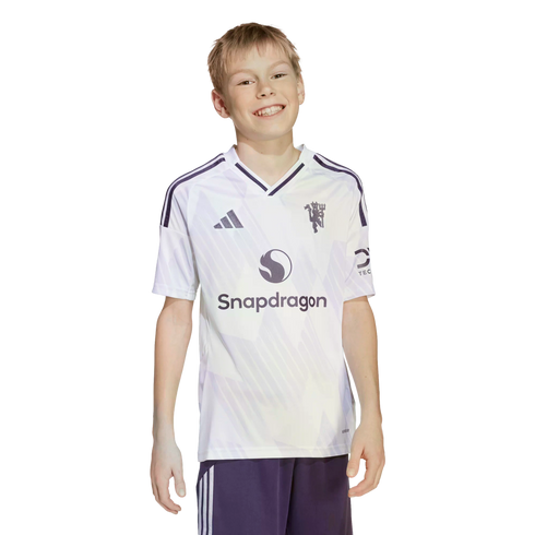 A smiling boy wearing a white and purple Manchester United soccer jersey with a Snapdragon logo, standing against a black background.