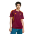 A man wearing a burgundy and orange AS Roma football jersey and blue jeans against a black background.