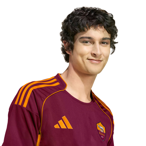 A young man with dark curly hair wearing a maroon and orange AS Roma soccer jersey, smiling against a black background.
