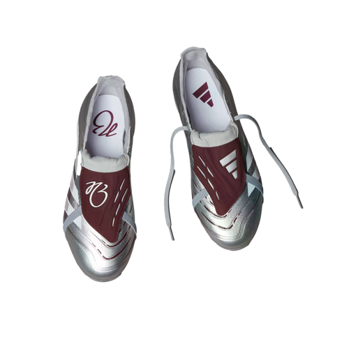 Top-down view of silver and maroon Adidas soccer cleats with metallic silver uppers, maroon fold-over tongues, and white laces against a plain white background.