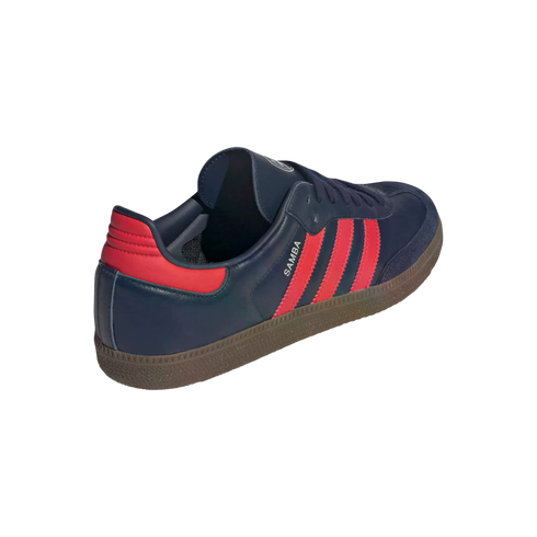 Rear-side view of a navy blue Adidas Samba sneaker with three red stripes, a red heel tab, and a brown gum rubber sole.