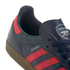 Close-up of a navy blue Adidas Samba sneaker featuring pink stripes and the Arsenal Football Club crest on the tongue.
