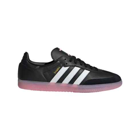 Profile view of a black Adidas Samba sneaker featuring three white stripes, gold lettering, and a translucent pink gum sole on a white background.