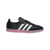 Profile view of a black Adidas Samba sneaker featuring three white stripes, gold lettering, and a translucent pink gum sole on a white background.