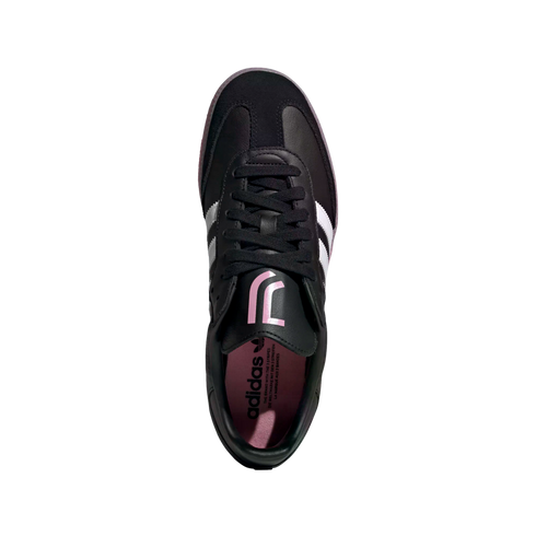 Top-down view of a black Adidas sneaker with three white stripes and a pink Juventus logo on the tongue. The shoe features black laces and a pink insole.