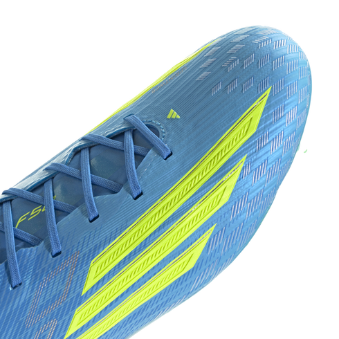 A close-up of a light blue Adidas F50 soccer cleat featuring three bold neon yellow stripes on the side. The shoe has a textured, ribbed upper with blue laces and a shimmering checkered pattern near the toe, shown against a black background.